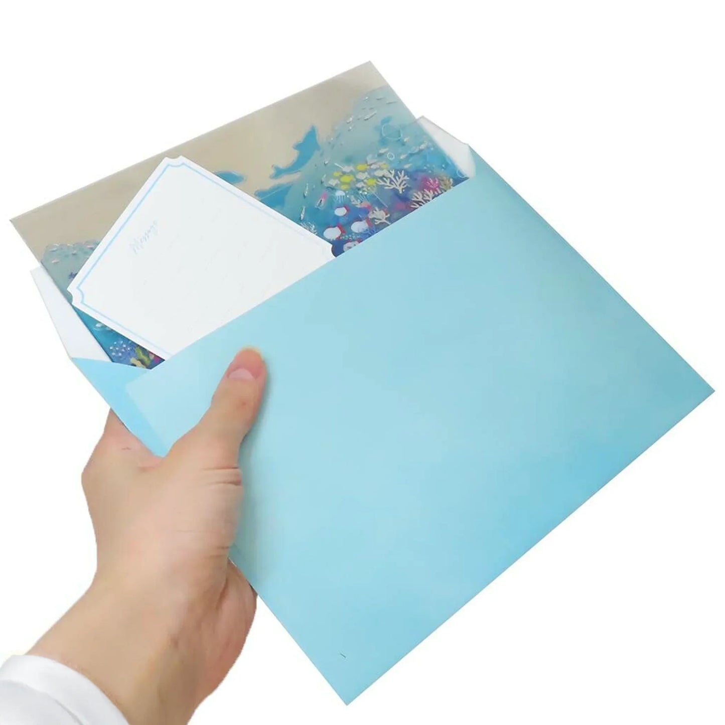 Hand holding a light blue envelope with Ocean Pop-Up Card – Holographic sea and fish design with waves – Summer greeting card inside on a white background