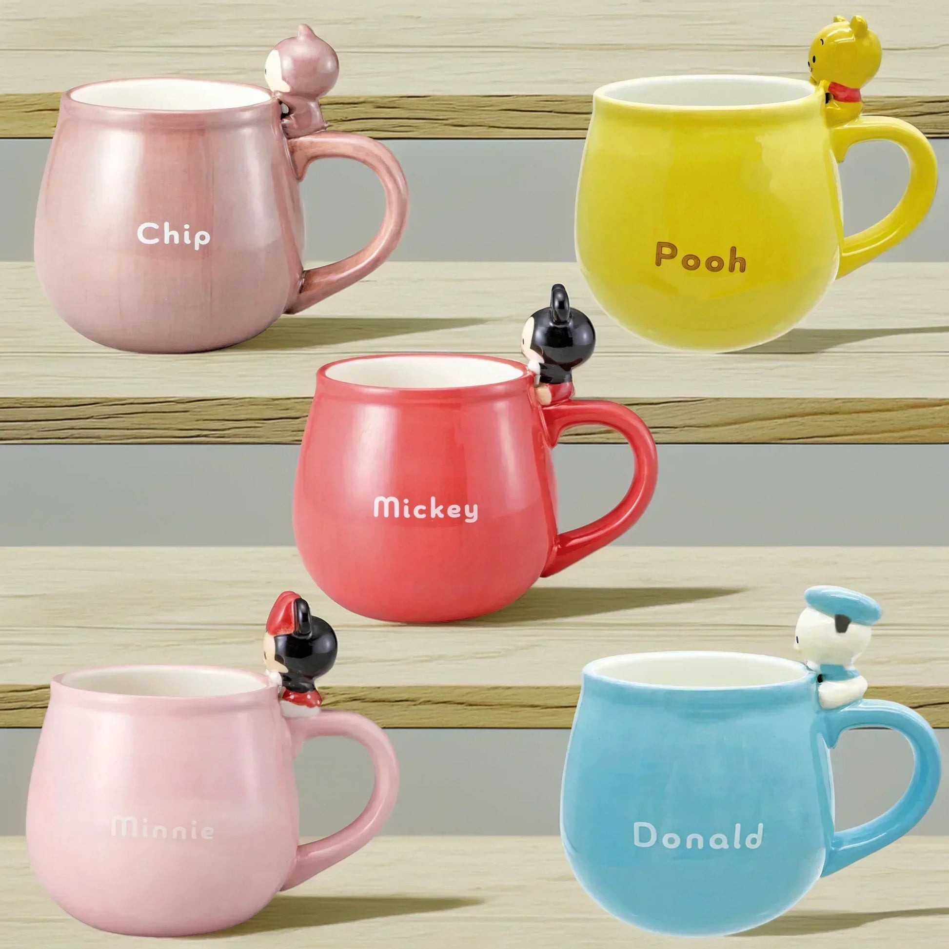 Set of colorful mugs with Disney character figurines on a wooden surface