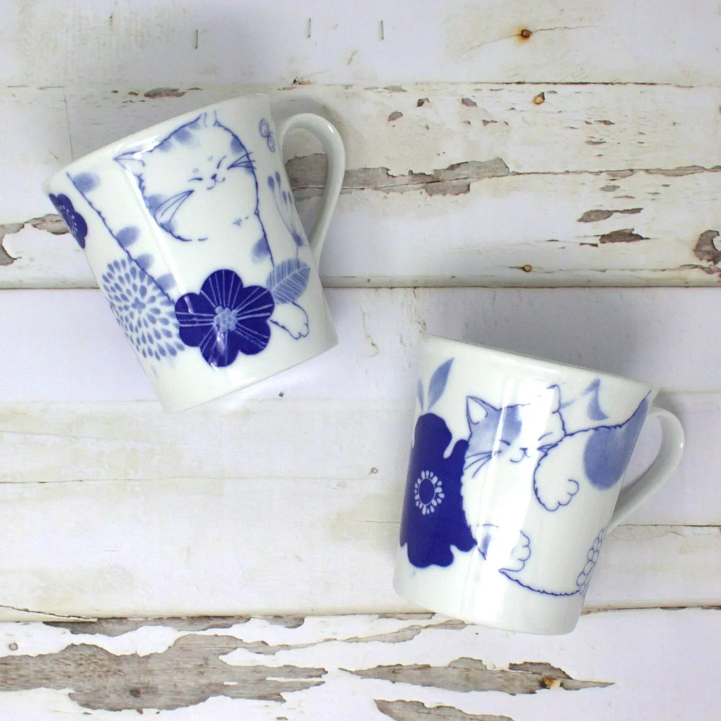 Japanese Nohohon Cat Porcelain Mug featuring Mugi and Sora with relaxed cat designs in blue and white.