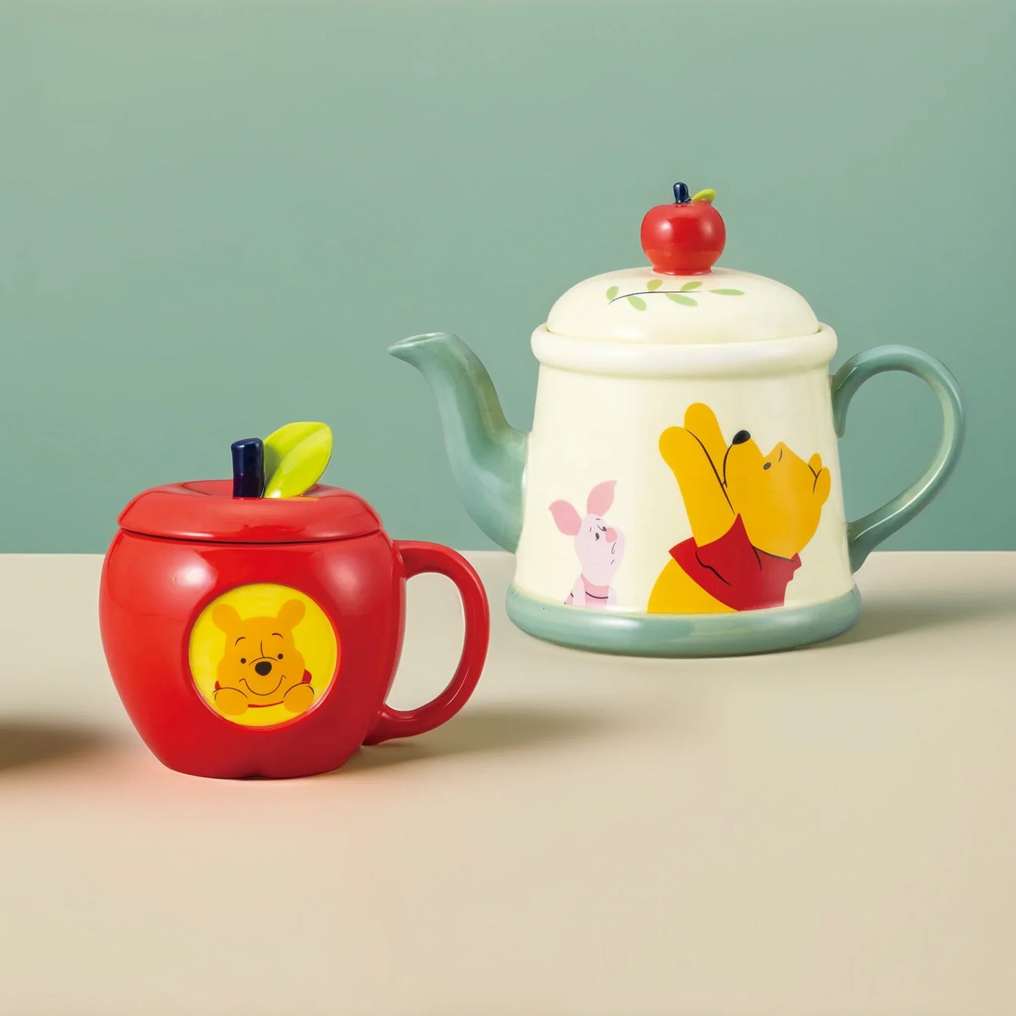 Winnie the Pooh porcelain apple mug with lid and matching teapot with apple handle on a pastel cream background – soft lighting, centered product display