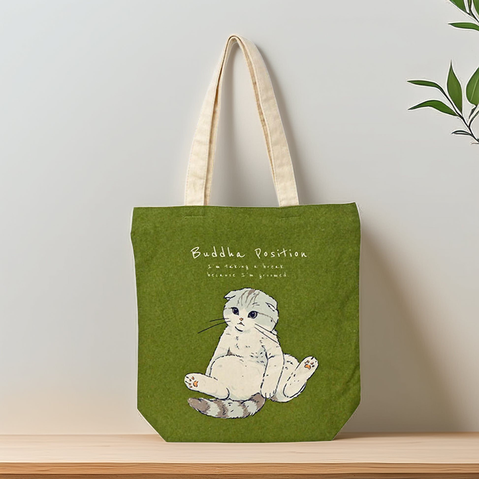 Green tote bag with a cat illustration and text on a wooden surface.