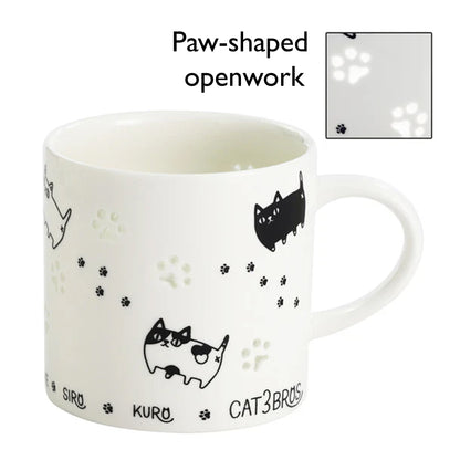 White mug with black cat illustrations and paw-shaped openwork on a white background