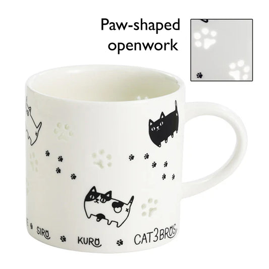 White mug with black cat illustrations and paw-shaped openwork on a white background